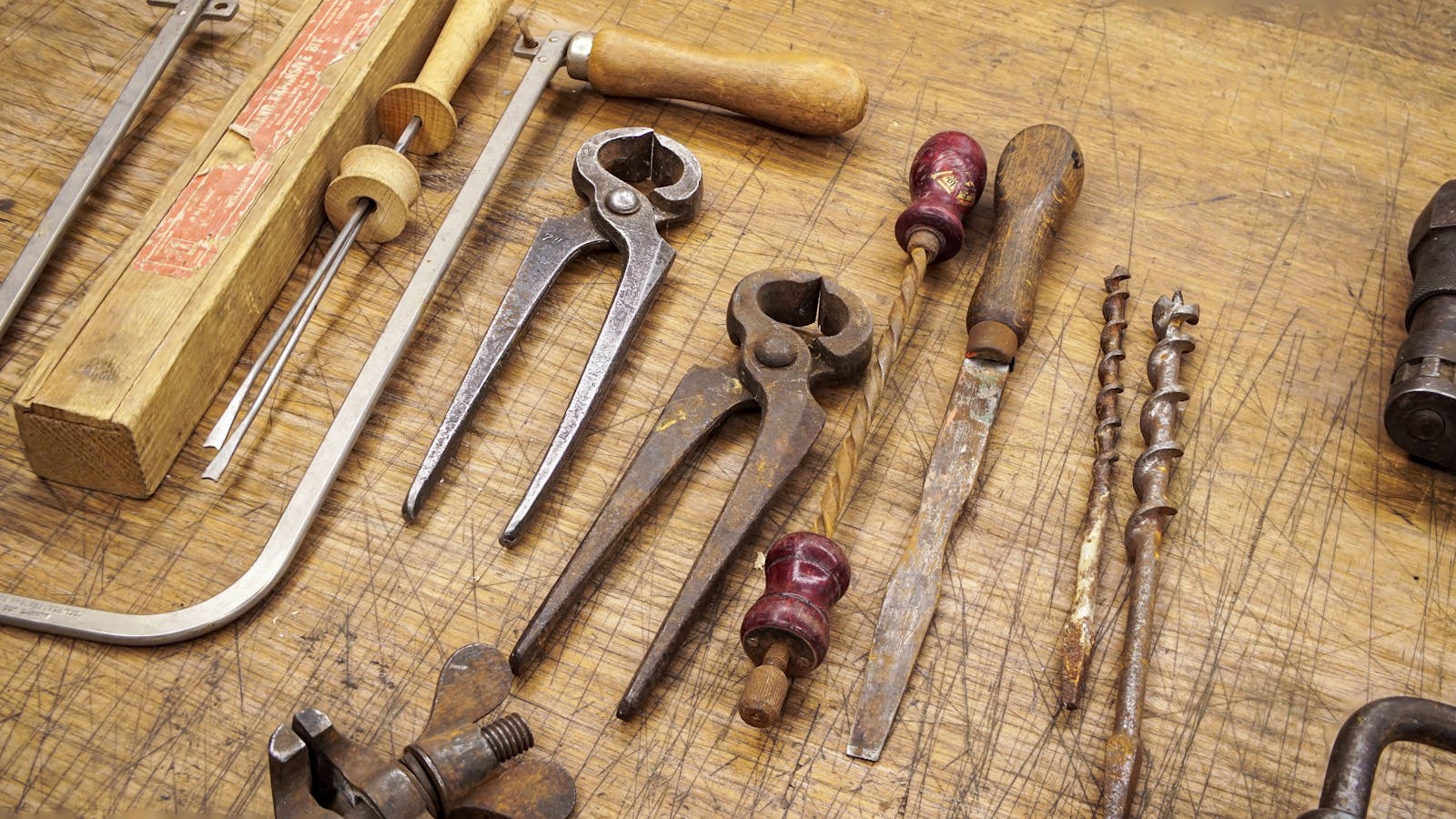 An assortment of rusty vintage hand tools on a worn wooden workbench