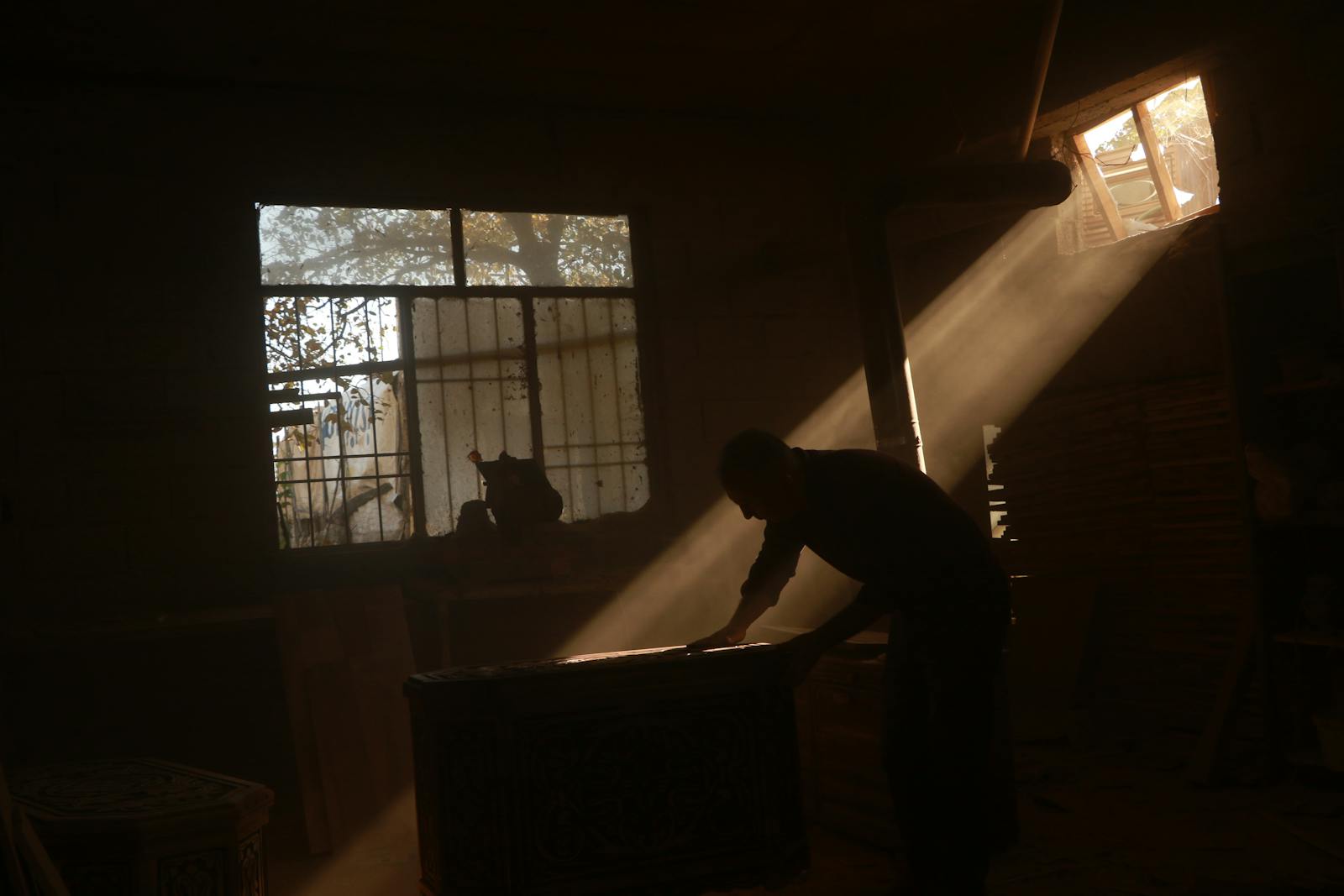Silhouette of a craftsman working in a sunlit workshop, dust motes catching light