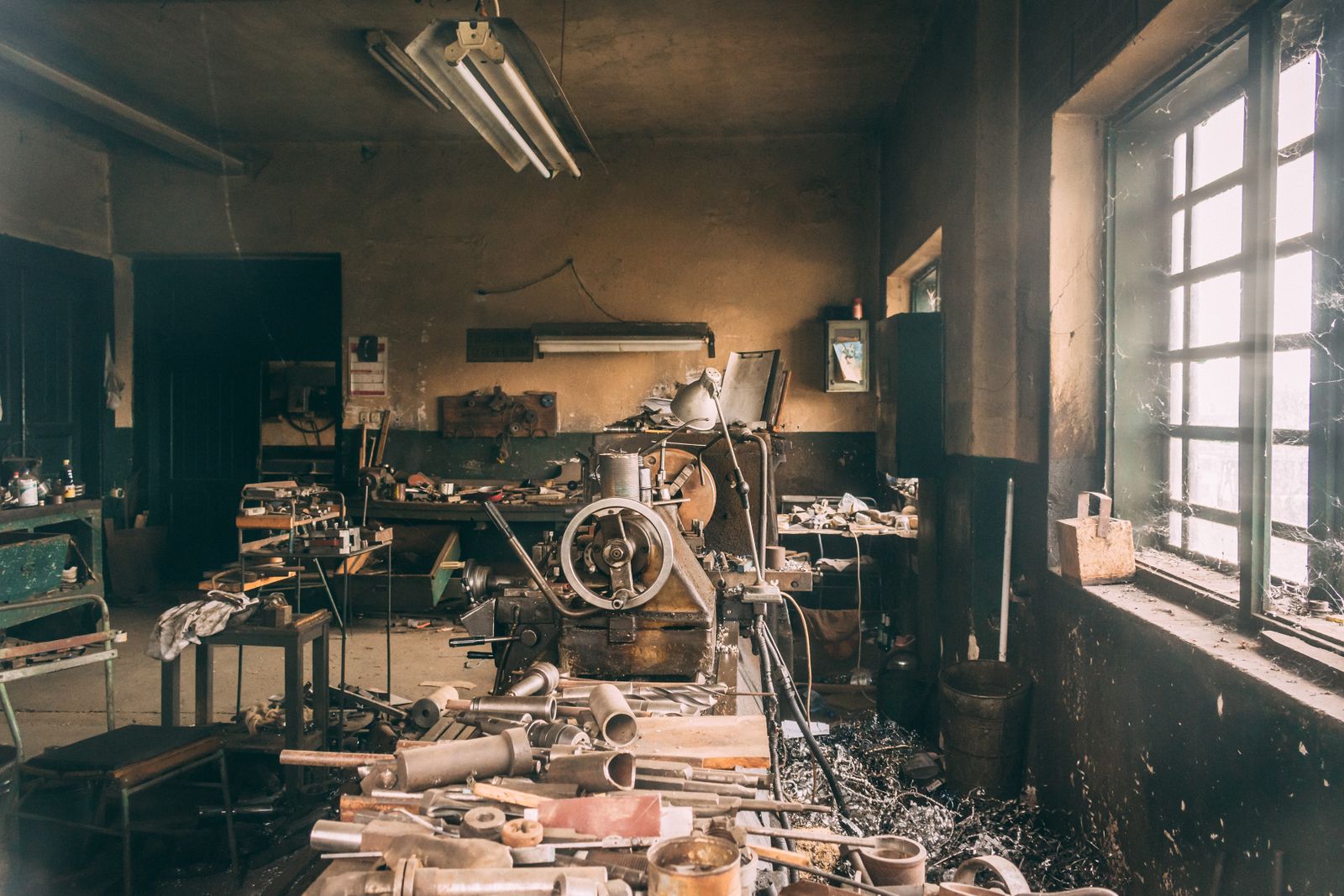 A weathered workshop interior — vintage lathe, scattered hand tools, window light