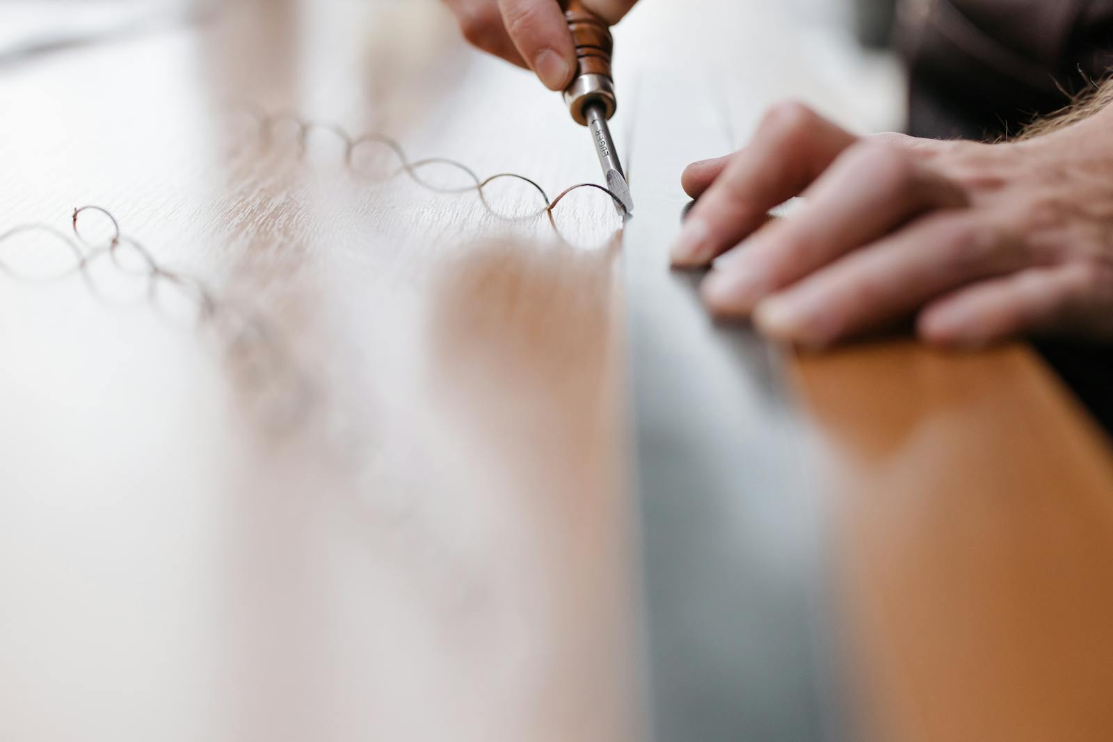 A craftsman's hands working a chisel against a wooden surface