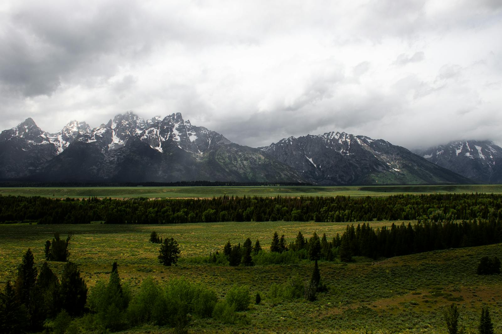 Snow-capped mountains with dramatic clouds over a green plain